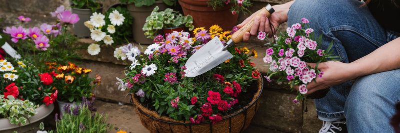 Person arranging flowers in a basket with a garden setting using a kent and stowe hand trowel