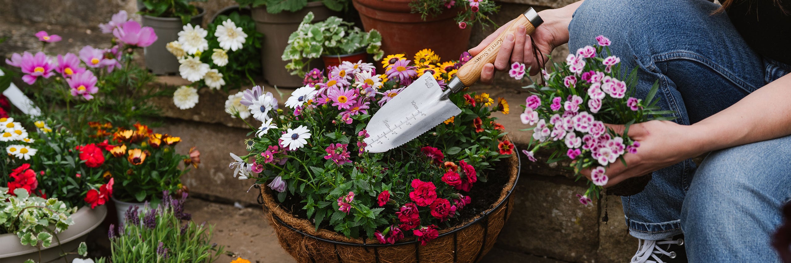 Person arranging flowers in a basket with a garden setting using a kent and stowe hand trowel